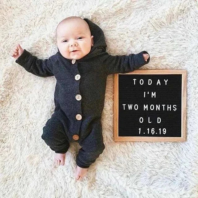 Baby in a cozy hooded romper next to a milestone board.